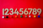 Illustrating the concept of real numbers decimal expansion, this image displays wooden numbers from 1 to 9 arranged horizontally on a red surface, with small, colorful blocks placed beneath each number.